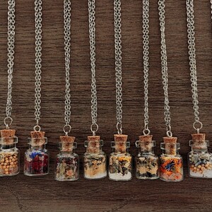 May include: Ten silver chain necklaces with small glass bottles filled with dried herbs and flowers. The bottles have cork stoppers.