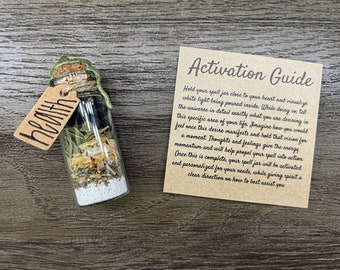 May include: A small glass jar filled with herbs and crystals, labeled "health" with a cork top and a green wax seal. Next to it is a card with the text "Activation Guide" and instructions for use.