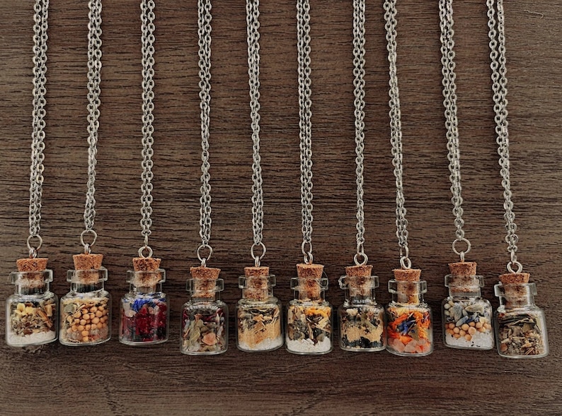 May include: Ten silver chain necklaces with small glass bottles filled with dried herbs and flowers. The bottles have cork stoppers.