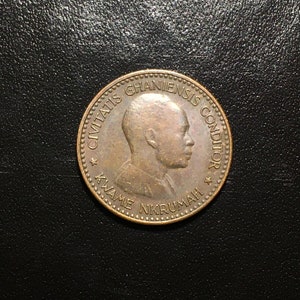 May include: A copper-colored coin with the inscription "CIVITATIS GHANIENSIS CONDITOR KWAME NKRUMAH" and a profile of a man on the front.