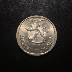 May include: A silver Finnish coin with the year 1983 and the text "SUOMEN TASAVALTA" around the edge. The coin features a lion with a sword in its paw.