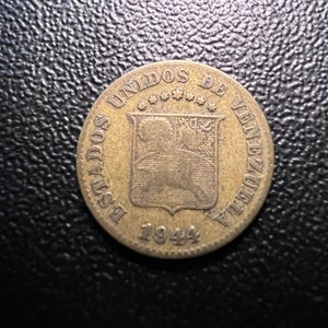 May include: A gold-colored coin with the inscription "Estados Unidos de Venezuela" and the year "1944" on the back. The coin features a shield with a tree and a horse.