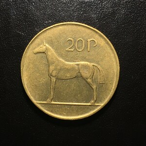 May include: A gold-colored 20 pence coin from Ireland featuring a horse profile on the front.