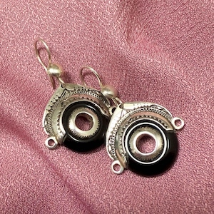 Puede incluir: Un par de pendientes de plata con piedras de ónix negro. Los pendientes son circulares y tienen diseños intrincados alrededor de las piedras.