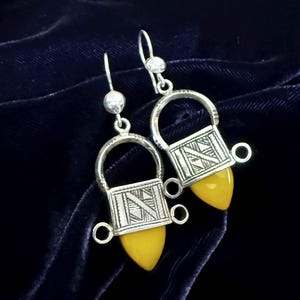 Puede incluir: Un par de pendientes de plata con una piedra amarilla y diseños geométricos intrincados. Los pendientes tienen la forma de una pequeña jaula con un fondo puntiagudo.