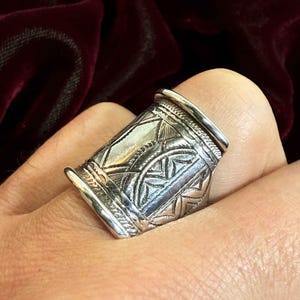 Könnte beinhalten: Ein silberner Ring mit einem komplizierten geometrischen Design. Der Ring ist breit und hat eine zylindrische Form.