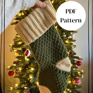 Puede incluir: Un calcetín navideño de ganchillo con cuerpo verde oliva oscuro y puño, talón y puntera acanalados de color crema. El calcetín incluye un lazo para colgar. Un gráfico circular blanco muestra el texto PDF Pattern en color negro.