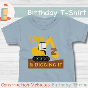 May include: A light blue t-shirt with a yellow construction vehicle graphic. The vehicle has a number "2" on the side and the text "I AM 2 & DIGGING IT".