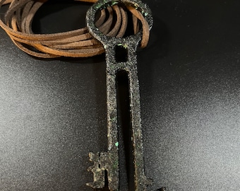 May include: A black metal key with a large circular loop at the top and two smaller keys attached to the bottom. The key has a distressed finish with green accents.