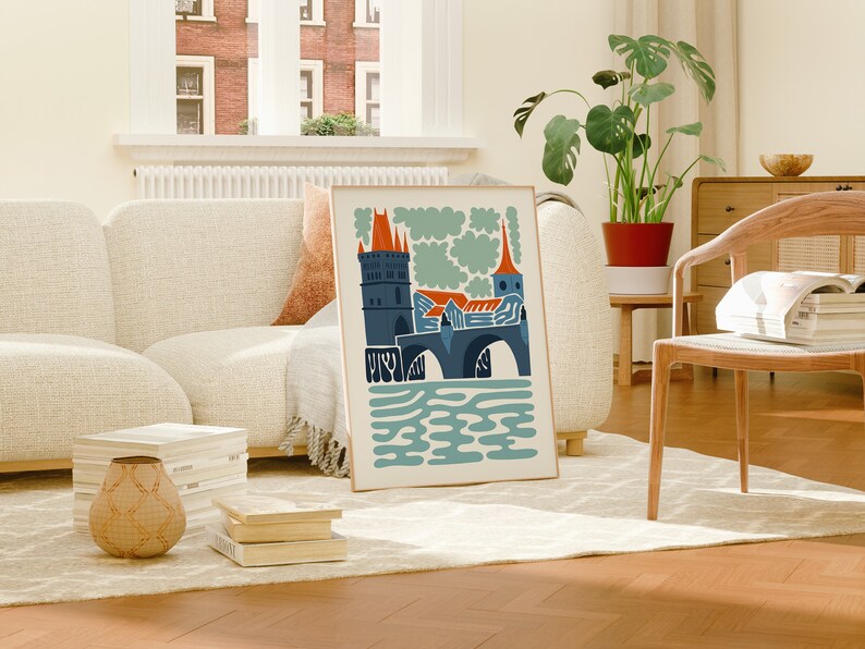 May include: A framed illustration of a bridge with a tower and a church in the background. The illustration is in a modern style with bold colours and simple shapes. The colours are blue, orange, and green.