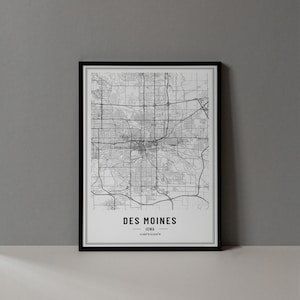 May include: A black and white map print of Des Moines, Iowa. The map shows the city's streets and landmarks. The text "Des Moines, Iowa 41.5868°N 93.6147°W" is printed below the map.