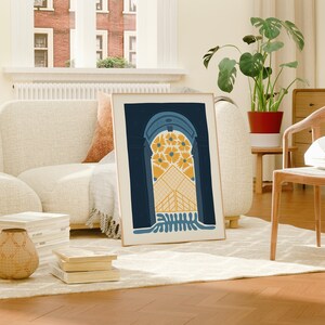 May include: A framed print of an abstract archway design with yellow and blue colors. The archway is filled with yellow flowers and a geometric pattern. The print is hanging on a wall in a living room setting.