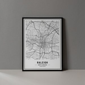 May include: A black and white map print of Raleigh, North Carolina, in a black frame. The map shows the city streets and landmarks. The text "Raleigh, North Carolina" is printed below the map.