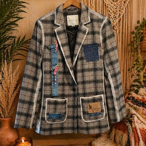 Op de afbeelding: Een geruite blazer in grijs, zwart en wit met denim patches en decoratieve details. De jas heeft een witte bies en twee voorzakken. Een patch op de blazer luidt "LIVE LIFE AUTHENTIC & TRUE".