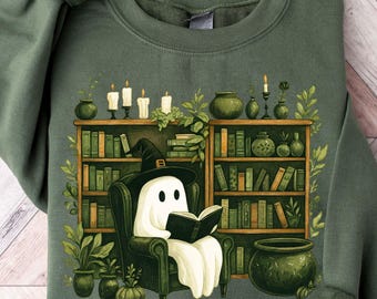 May include: Green sweatshirt featuring a whimsical illustration of a ghost reading in a cozy library setting. The design includes bookshelves, candles, and a cauldron, creating a spooky yet inviting atmosphere. The ghost wears a witch hat and is seated in a green armchair.