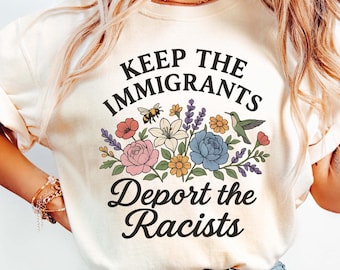 May include: Cream-colored t-shirt with the text "KEEP THE IMMIGRANTS, Deport the Racists" in black script. The shirt features a floral design with a bee, hummingbird, and various flowers in pink, blue, and yellow.