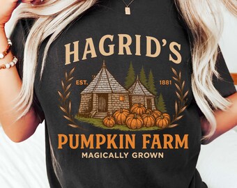 May include: Black t-shirt featuring the text "Hagrid's Pumpkin Farm" with an illustration of a cottage and pumpkins. The design includes the text "Magically Grown" and "Est. 1881".