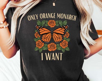 May include: Black t-shirt featuring a monarch butterfly design with orange and black wings, surrounded by orange roses. The text "ONLY ORANGE MONARCH I WANT" is printed above and below the butterfly illustration.