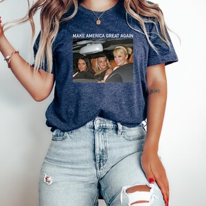 Puede incluir: Una camiseta azul marino con un gr&aacute;fico blanco de tres mujeres en un coche. El texto "MAKE AMERICA GREAT AGAIN" est&aacute; impreso sobre el gr&aacute;fico.