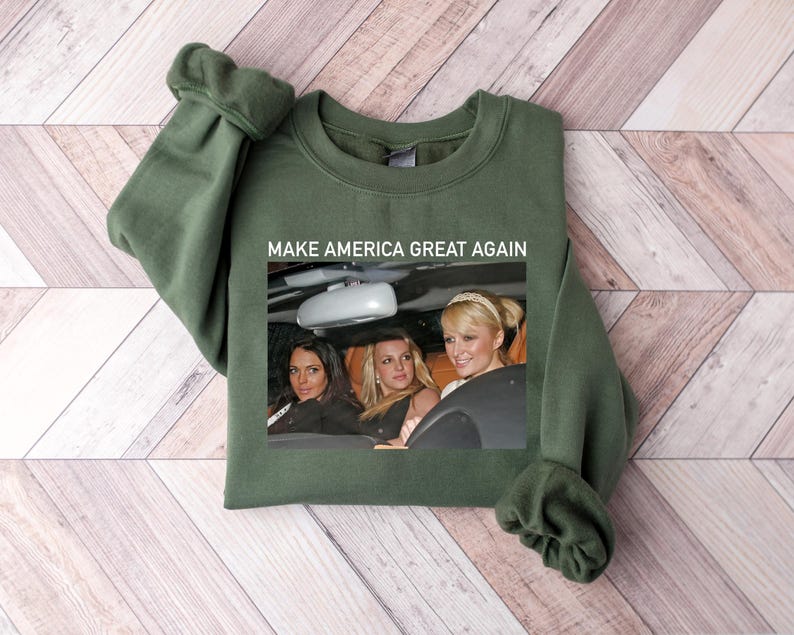 Puede incluir: Una sudadera verde oscuro con el texto "Make America Great Again" impreso en la parte delantera. La sudadera presenta una foto de tres mujeres en un coche.