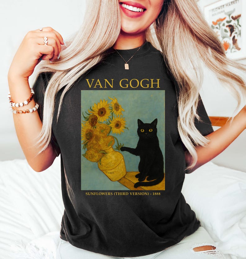 May include: Black t-shirt featuring a print of Van Gogh's "Sunflowers" with a black cat. The design includes the text "VAN GOGH" above the image and "SUNFLOWERS (THIRD VERSION) - 1888" below. The artwork depicts sunflowers in a vase.