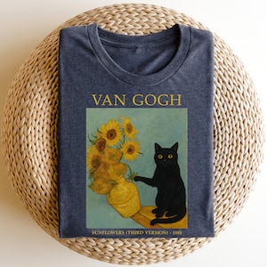 May include: A navy blue t-shirt featuring a graphic of Van Gogh's "Sunflowers" painting with a black cat. The text "VAN GOGH" is above the image, and "SUNFLOWERS (THIRD VERSION) - 1888" is below.