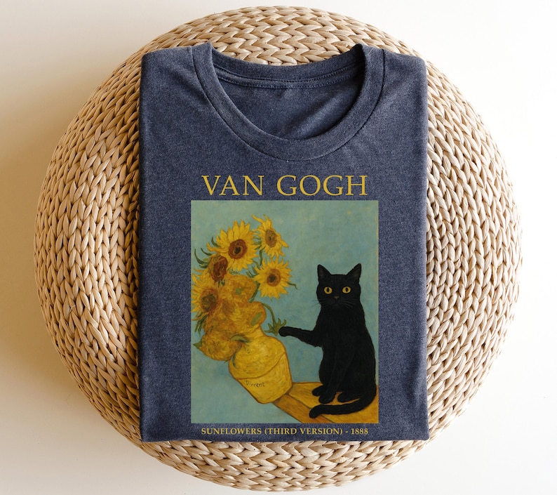 May include: A navy blue t-shirt featuring a graphic of Van Gogh's "Sunflowers" painting with a black cat. The text "VAN GOGH" is above the image, and "SUNFLOWERS (THIRD VERSION) - 1888" is below.