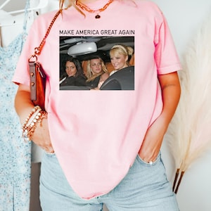 Puede incluir: Camiseta rosa con el texto "MAKE AMERICA GREAT AGAIN" y una foto de tres mujeres en un coche.