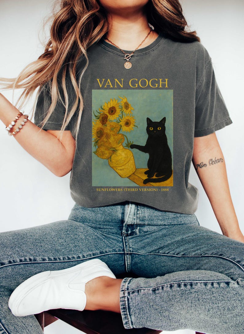 May include: Dark gray t-shirt featuring a print of Van Gogh's "Sunflowers (Third Version)" painting with a black cat. The text "VAN GOGH" is above the image, and "SUNFLOWERS (THIRD VERSION) - 1888" is below.