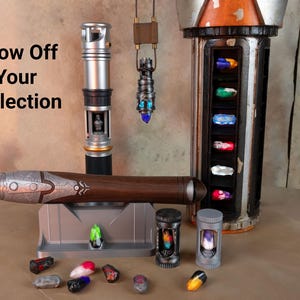 K&ouml;nnte beinhalten: Eine Sammlung von Lichtschwertern und Zubeh&ouml;r wird pr&auml;sentiert. Das Bild zeigt ein silbernes und schwarzes Lichtschwert, ein braunes und silbernes Lichtschwert und einen h&auml;ngenden Anh&auml;nger. Es gibt auch verschiedene farbige Kristalle und Beh&auml;lter mit dem Text "Show Off Your Collection".