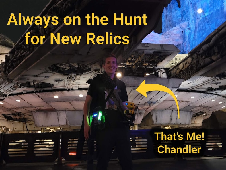K&ouml;nnte beinhalten: Eine Person steht vor einer gro&szlig;en Raumschiffstruktur und h&auml;lt einen kleinen gelb-schwarzen Droiden. Das Bild enth&auml;lt den Text "Always on the Hunt for New Relics" und "That's Me! Chandler". Die Szene wird von blauen und gr&uuml;nen Lichtern beleuchtet.