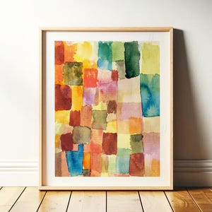 May include: Abstract watercolor painting in a wooden frame. The artwork features a grid of colorful, irregular rectangles in shades of red, orange, yellow, green, blue, and purple. The painting is displayed on a wooden floor.