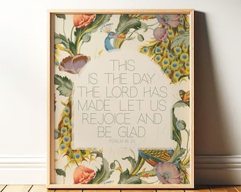 May include: A framed print with a floral and peacock feather design. The text reads "THIS IS THE DAY THE LORD HAS MADE LET US REJOICE AND BE GLAD" from Psalm 118:24. The frame is made of light-colored wood.