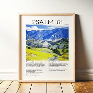 May include: Framed art print featuring the text "PSALM 61" above a landscape painting of rolling green hills and blue mountains. The print includes biblical text below the image, all within a light wood frame.