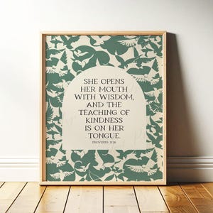 May include: A framed print with a light wood frame. The artwork features a cream-colored background with a pattern of green birds. The text reads, "SHE OPENS HER MOUTH WITH WISDOM, AND THE TEACHING OF KINDNESS IS ON HER TONGUE. PROVERBS 31:26."