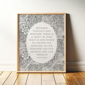 May include: Framed print with a light wood frame. The print features a floral pattern in black and white surrounding an oval with the quote: "Between stimulus and response there is a space..." by Viktor Frankl.