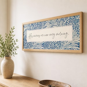 May include: A rectangular wall sign in a light wood frame featuring a blue and white floral pattern surrounding a central cream-colored panel with the black cursive text, His mercies are new every morning, printed in the center of the artwork.
