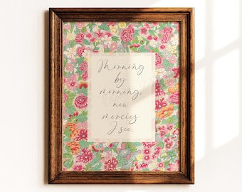 May include: A rectangular dark wood frame holds a print featuring a dense floral pattern of pink, red, orange, and yellow flowers on a light green background. Centered is a white rectangle with the text Morning by morning, new mercies I see.