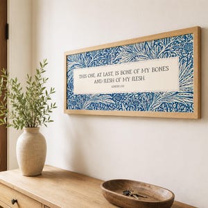 May include: A rectangular wall art piece in a light wood frame featuring a blue and white floral pattern background with a central cream-colored rectangular insert containing the text: THIS ONE, AT LAST, IS BONE OF MY BONES AND FLESH OF MY FLESH. GENESIS 2:23.
