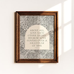 Op de afbeelding: Ingelijste kunst met de quote "ABOVE ALL, LOVE EACH OTHER DEEPLY, BECAUSE LOVE COVERS OVER A MULTITUDE OF SINS." De print heeft een bloemenpatroon achtergrond en een donkerbruine houten lijst.