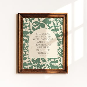 May include: A framed print with a wooden frame. The print features a green and white bird pattern background. The text reads: "SHE OPENS HER MOUTH WITH WISDOM, AND THE TEACHING OF KINDNESS IS ON HER TONGUE. PROVERBS 31:26."