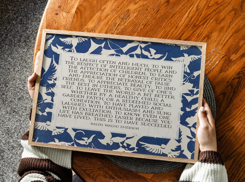 May include: A framed print featuring a quote by Ralph Waldo Emerson, surrounded by a blue and white bird pattern. The text is in a classic serif font. The frame is made of light-colored wood. The quote is about success.