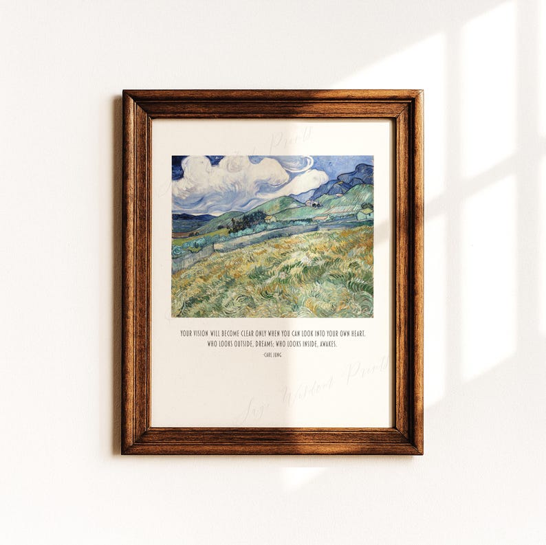 May include: A framed art print featuring a landscape painting with rolling green hills, a blue sky with white clouds, and a stone wall. Below the image, the text reads: YOUR VISION WILL BECOME CLEAR ONLY WHEN YOU CAN LOOK INTO YOUR OWN HEART. WHO LOOKS OUTSIDE, DREAMS; WHO LOOKS INSIDE, AWAKES. CARL JUNG.
