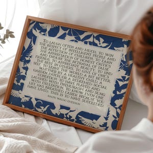 May include: A framed print featuring a quote by Ralph Waldo Emerson. The print has a cream-colored background with a blue floral pattern border. The text is in black, and the frame is a light brown color.