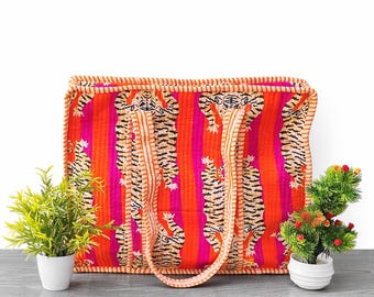 May include: A rectangular quilted tote bag featuring a vibrant pattern of orange and pink vertical stripes with repeating tiger illustrations. The bag has two matching striped fabric handles and orange and white striped piping along the edges.