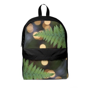 May include: Black backpack with a green fern leaf design on a blurred background of golden lights.