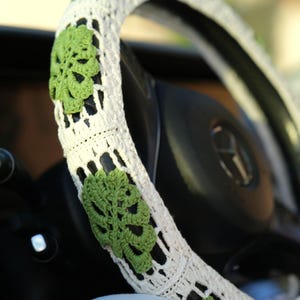 Detailed close-up of green Monstera leaves crocheted onto a white steering wheel cover.