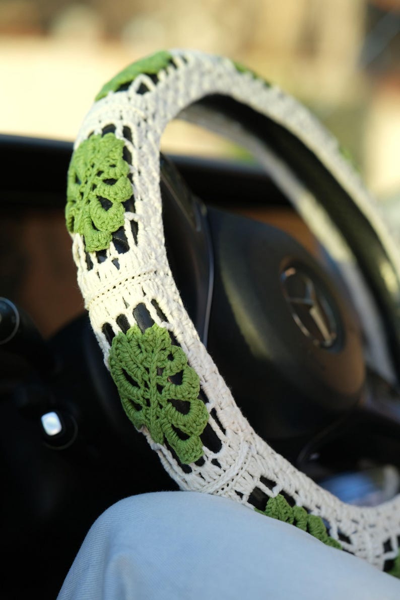 Detailed close-up of green Monstera leaves crocheted onto a white steering wheel cover.