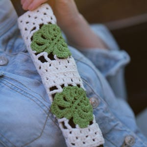 White crochet seat belt cover with green Monstera leaf appliques shown worn across the shoulder.
