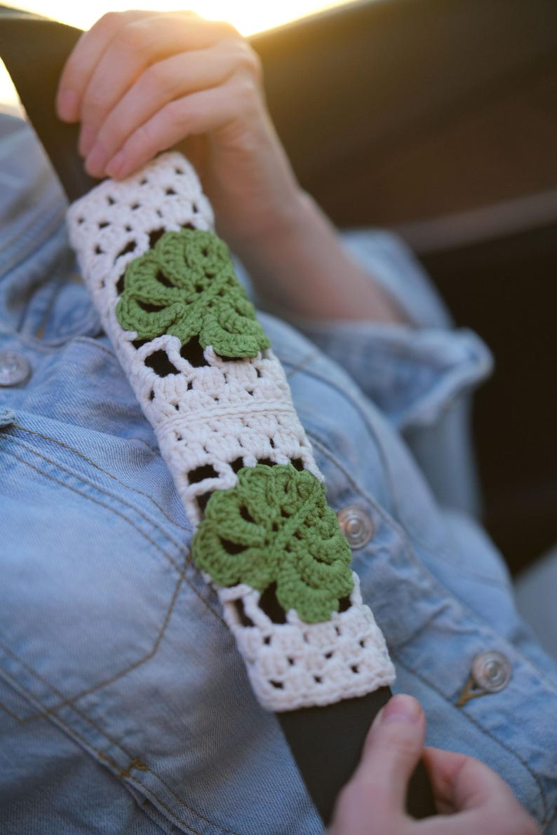 White crochet seat belt cover with green Monstera leaf appliques shown worn across the shoulder.